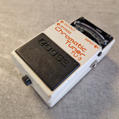 Pre-Owned Boss TU-3 Tuner Pedal A vintage BOSS TU-3 Chromatic Guitar Tuner pedal, featuring a white metal casing with orange lettering and a black footswitch, resting on a gray textured surface.