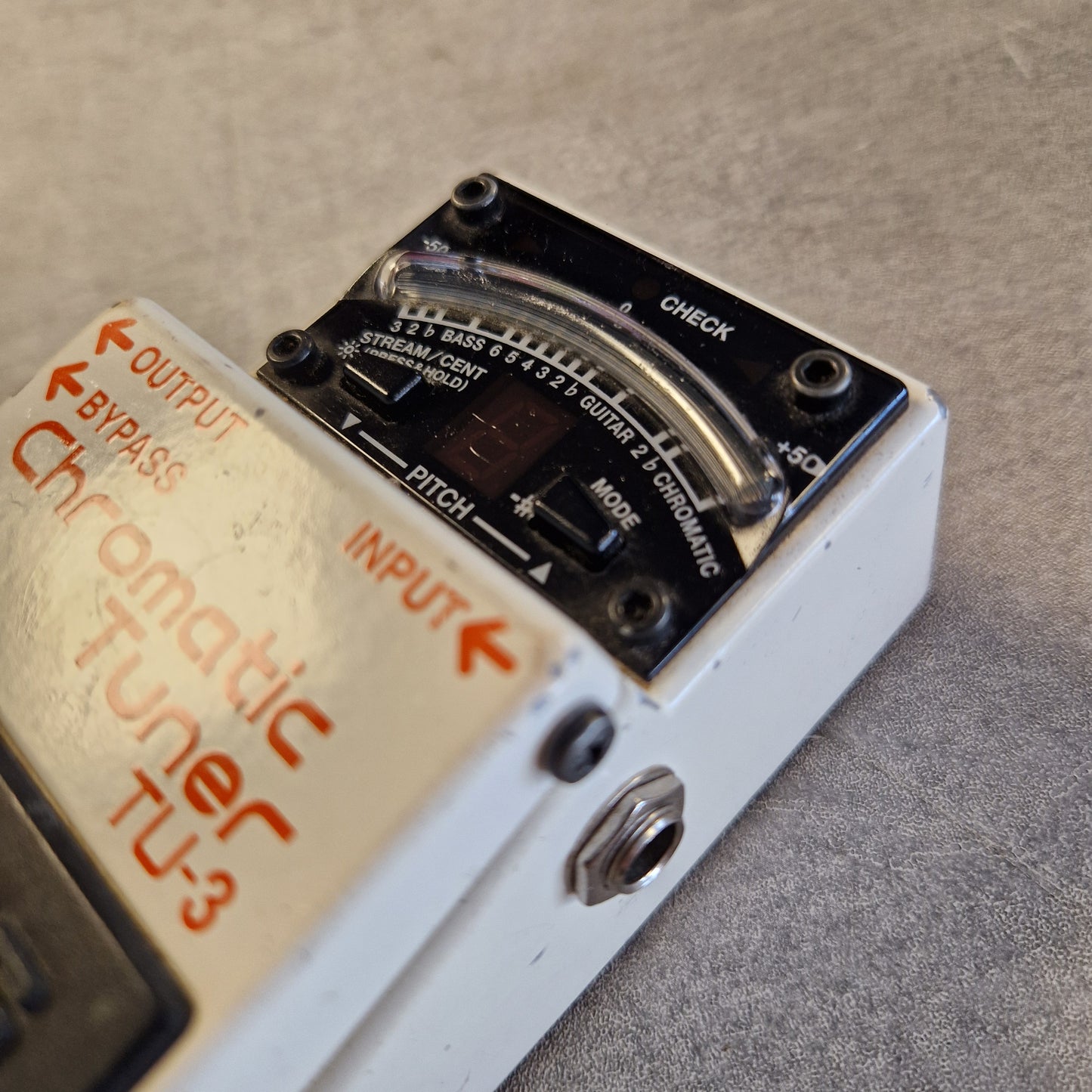 Pre-Owned Boss TU-3 Tuner Pedal Close-up of a white and black Fuzz Face II chromatic guitar tuner with the TU-3 model name printed on the front, set against a gray textured background.