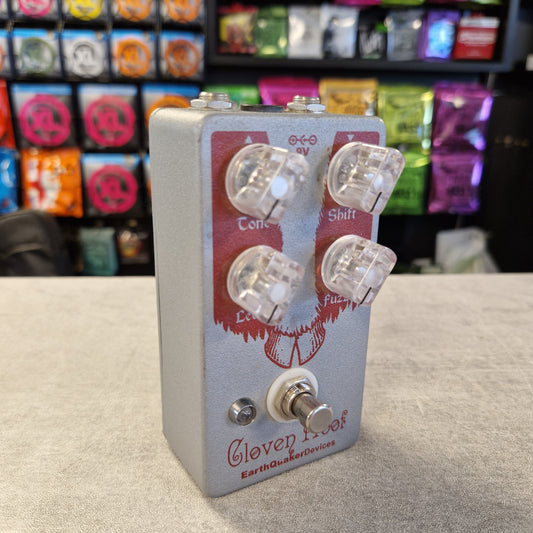 Pre-Owned EarthQuaker Devices Cloven Hoof Fuzz Pedal A Gloep Tree Earthquake Effects pedal guitar effect unit with a silver-gray metal casing, red and white graphic design, and four clear knobs, set on a gray tabletop with a blurred store background.