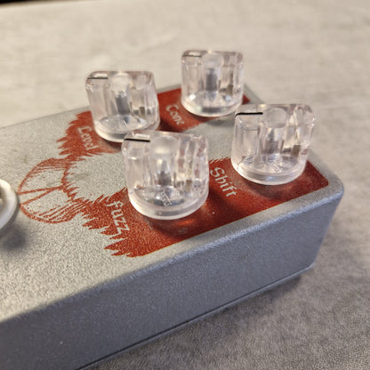 Pre-Owned EarthQuaker Devices Cloven Hoof Fuzz Pedal A close-up of a guitar effects pedal with a textured gray body, red printed graphics, and four clear acrylic knobs labeled Gain, FX1, FX2, and Com.