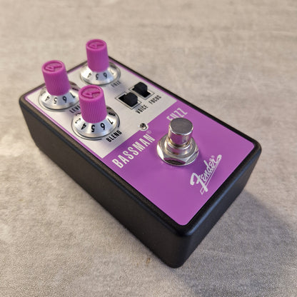 Pre-Owned Fender Bassman Fuzz Pedal Fender Bassman EZ72 bass guitar effects pedal with a black body, purple control panel, and pink knobs, shown on a textured gray surface.