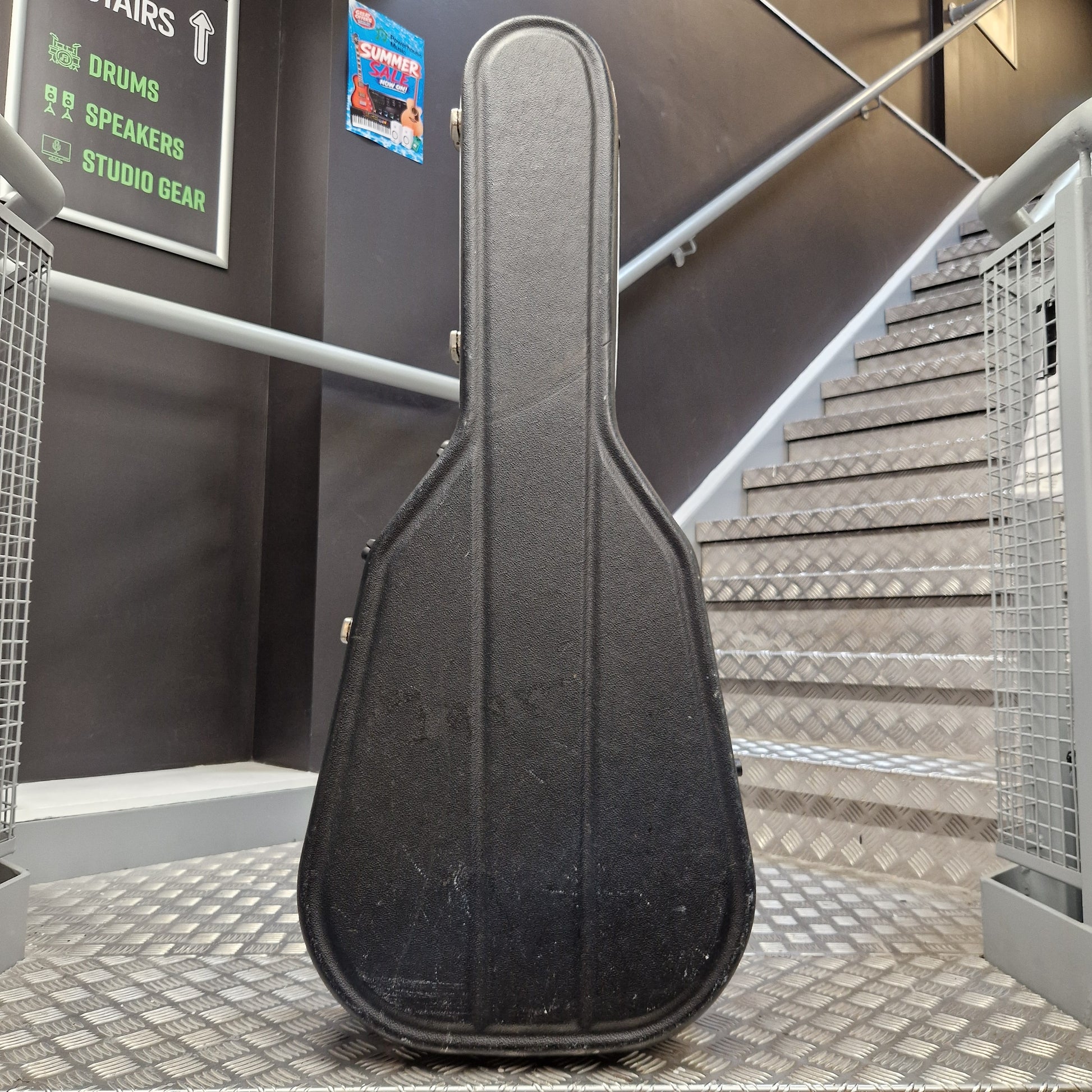 Pre-Owned Hiscox LiteFlite Acoustic Hard Case A black hard guitar case standing upright on a metal staircase landing in an indoor studio or building setting.