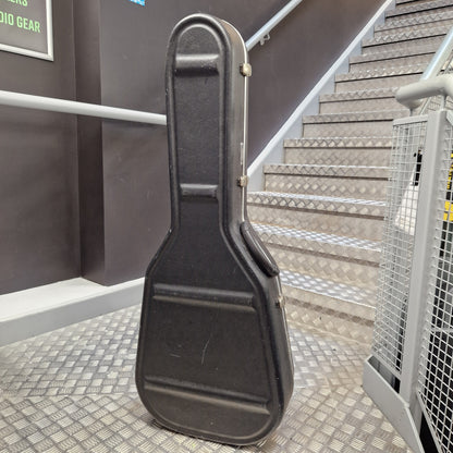 Pre-Owned Hiscox LiteFlite Acoustic Hard Case A black hard guitar case standing upright on a metal treadmill staircase in an indoor setting.