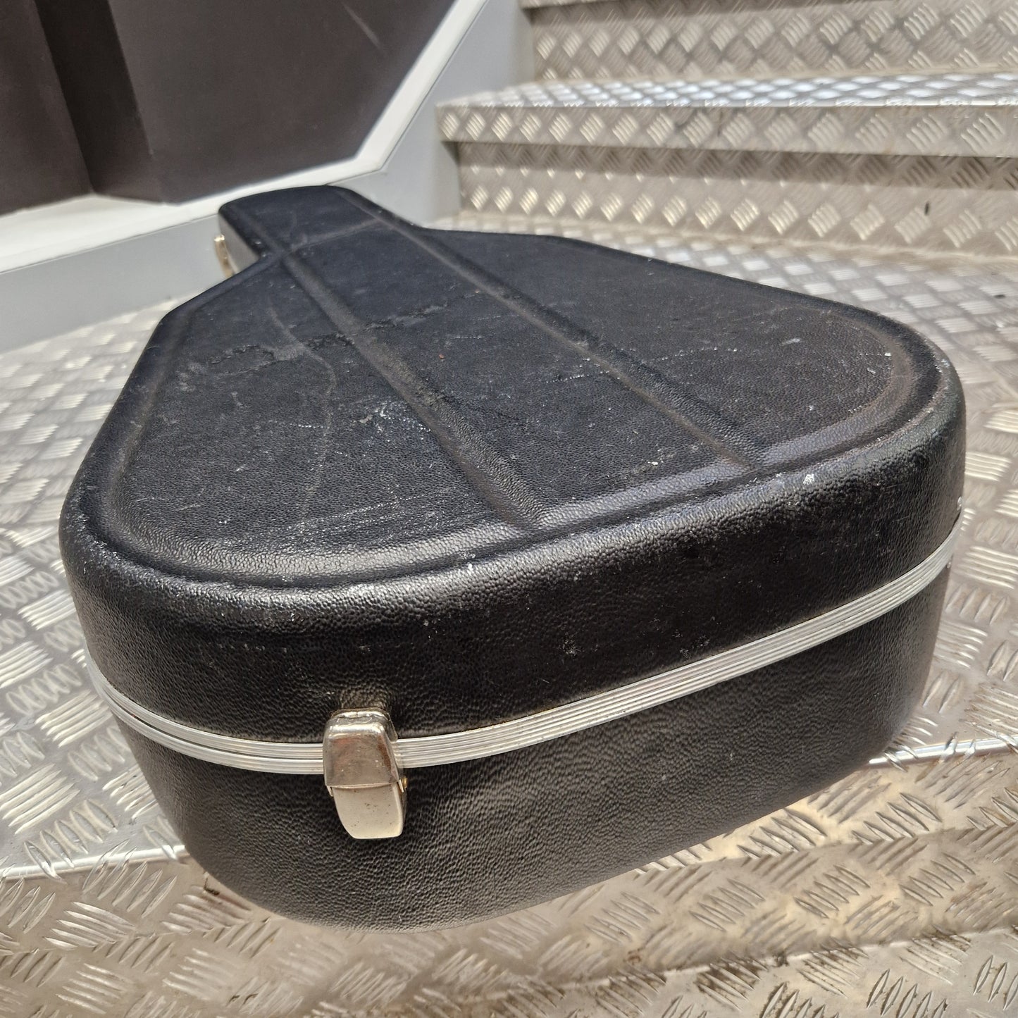 Pre-Owned Hiscox LiteFlite Acoustic Hard Case A black hard guitar case with a silver metal zipper and latch, resting on a diamond plate metal staircase.