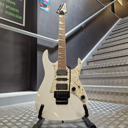 Pre-Owned Ibanez RG350DX Electric - White A white electric guitar with a black bridge and pickups, displayed on a stand in front of a staircase.