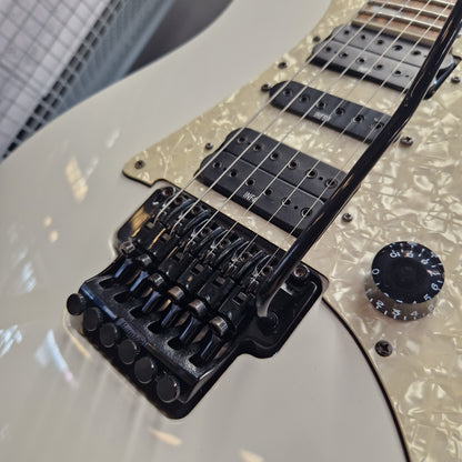 Pre-Owned Ibanez RG350DX Electric - White Close-up of an electric guitar body showing a glossy white finish, a pearlescent cream pickguard, black humbucker pickups, and a black bridge system with multiple saddles.