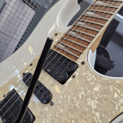 Pre-Owned Ibanez RG350DX Electric - White Close-up of an electric guitar body showing a cream-colored faceted pearlescent pickguard, black humbucker pickups, a maple fretboard, and part of a white body shell.