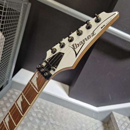 Pre-Owned Ibanez RG350DX Electric - White Close-up of an Ibanez electric guitar headstock and neck, showing the white headstock with black logo, tuning pegs, and a brown fretboard in a real indoor setting.