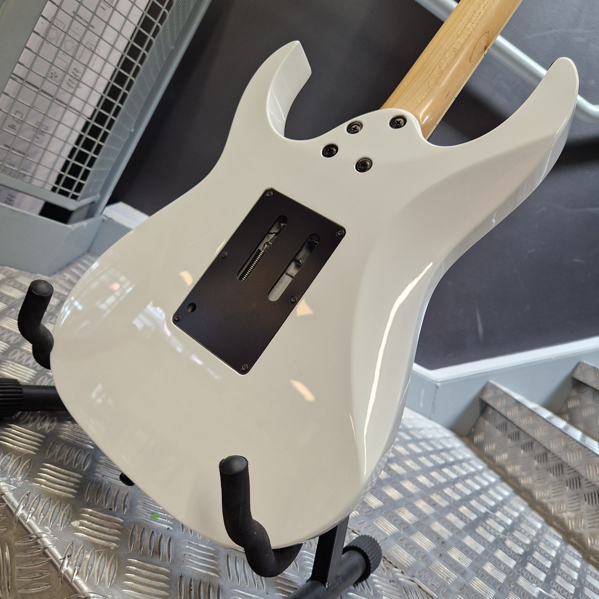 Pre-Owned Ibanez RG350DX Electric - White A close-up of a white electric guitar body on a stand, showing the back plate, black pickup cover, control holes, and part of a natural wood neck.