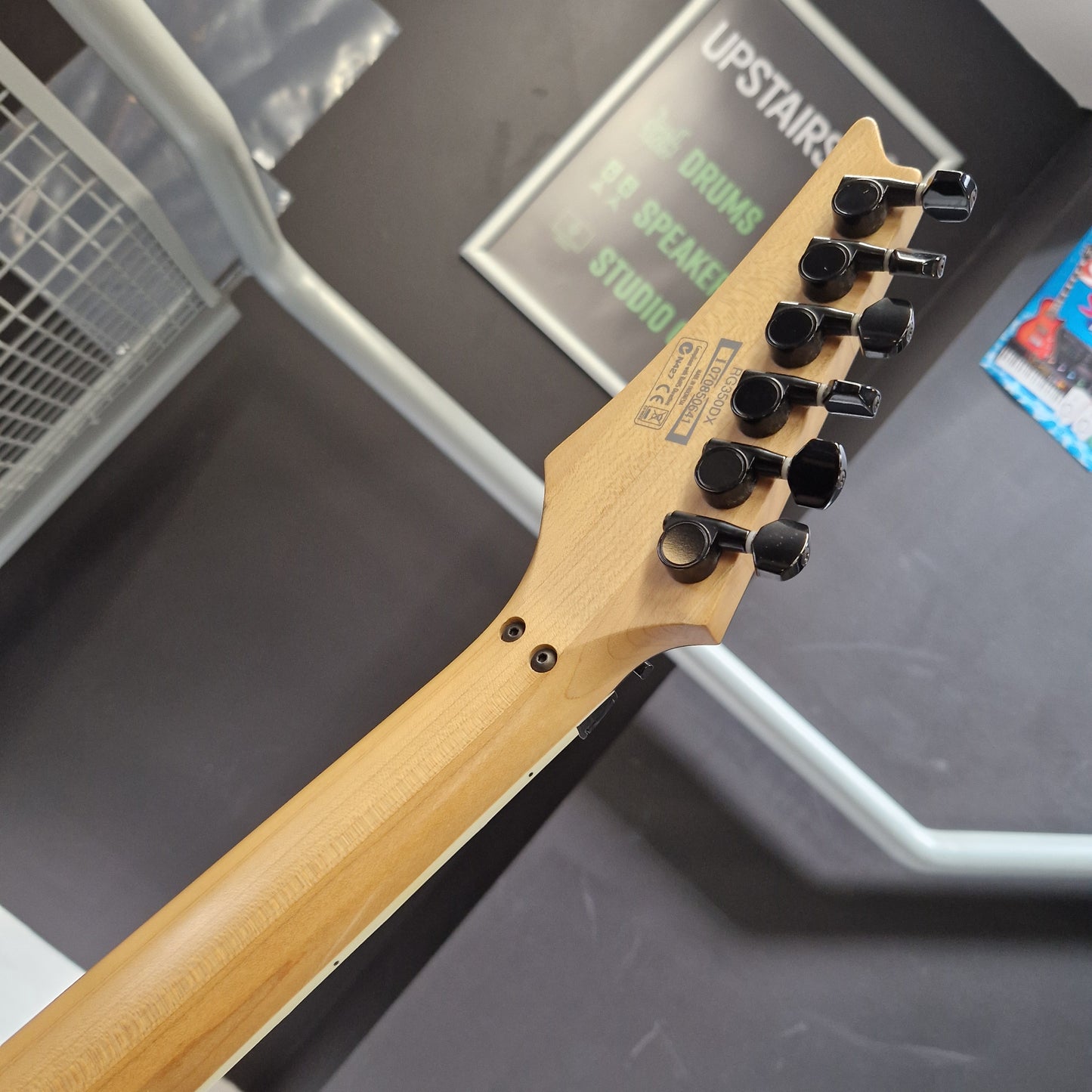 Pre-Owned Ibanez RG350DX Electric - White Close-up of the headstock and neck of an electric guitar, showing a natural wood finish and black tuning pegs, photographed in a studio or showroom setting.