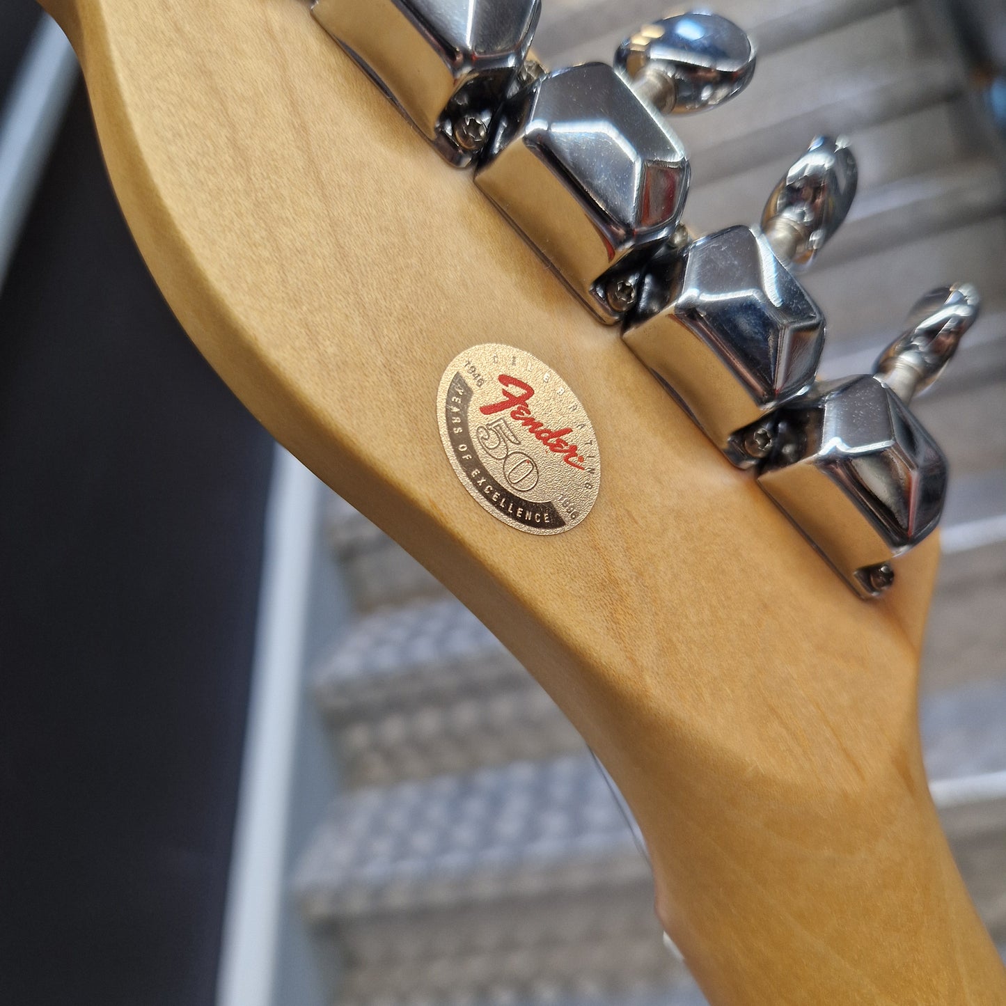 Pre-Owned Squier MIK 1996 Telecaster Electric - Blonde Close-up of a Fender bass guitar headstock showing the maple wood neck, chrome tuning pegs, and a round 50th anniversary sticker.