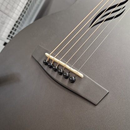 Pre-Owned Enya Nova Go SP1 Carbon Fibre Electro-Acoustic - Matte Black Close-up of a guitar's bridge and strings, showing a matte dark gray body, cream-colored bridge bar, and black tuning pegs.
