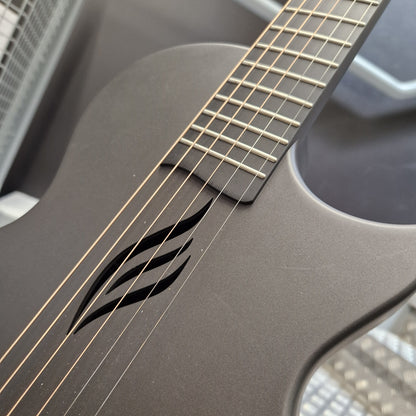 Pre-Owned Enya Nova Go SP1 Carbon Fibre Electro-Acoustic - Matte Black Close-up of a matte black electric guitar showing the neck, strings, and a distinctive black wave-like inlay on the body.