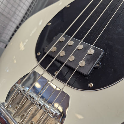 Pre-Owned Music Man Sterling Sub Series Ray 4 Bass - White Close-up of a bass guitar body showing a cream-colored finish, a black pickguard, silver hardware, and part of a black humbucker pickup with metal pole pieces.