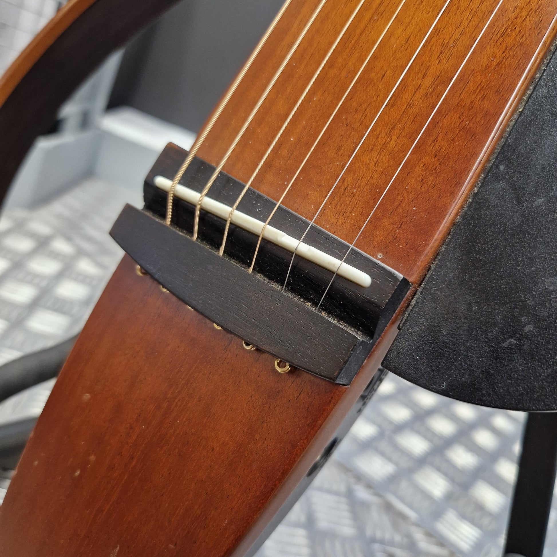 Pre-Owned Yamaha SLG200S Silent Guitar Electro-Acoustic - Natural Close-up of a six-string acoustic guitar showing the dark wood bridge, white saddle, and warm brown wooden body.