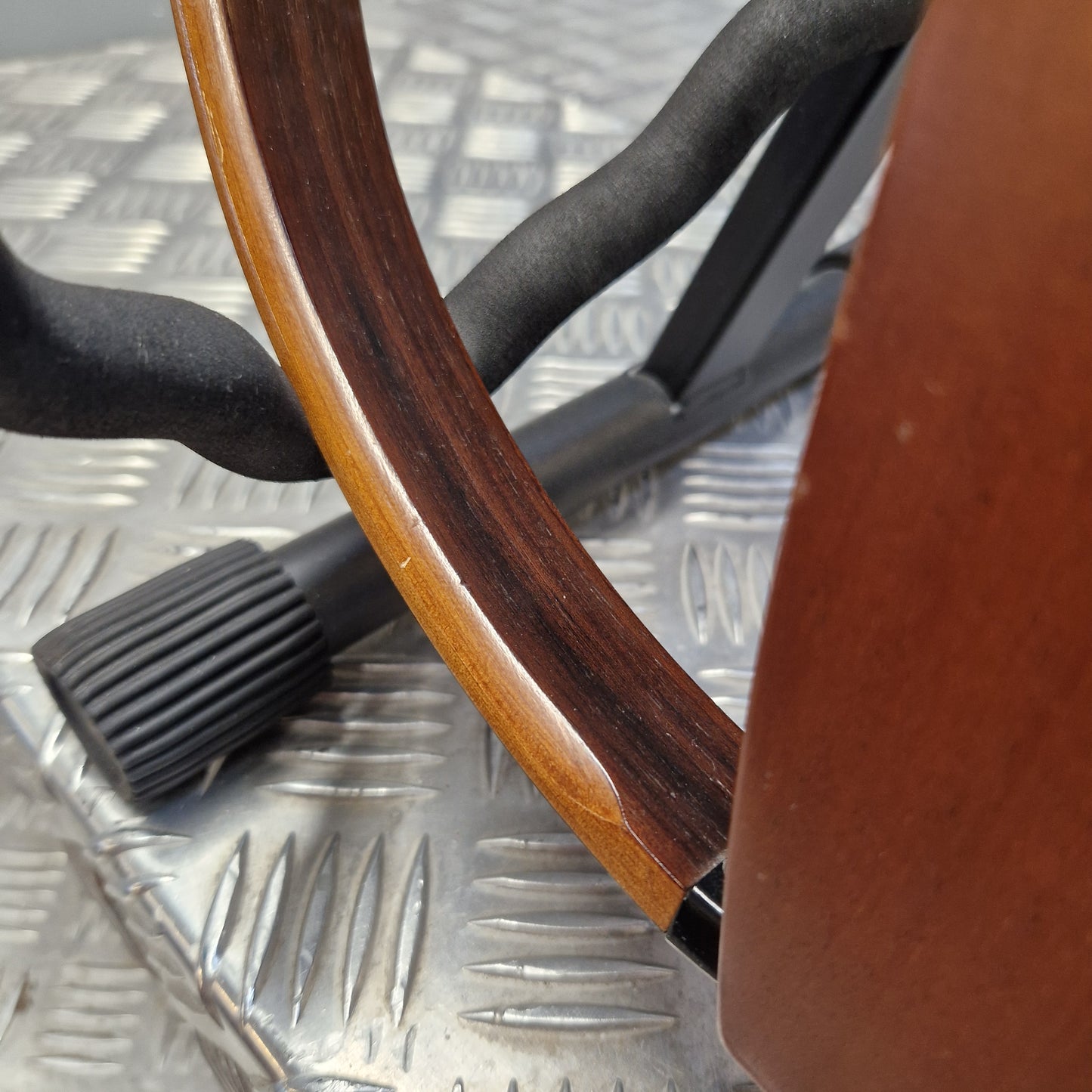Pre-Owned Yamaha SLG200S Silent Guitar Electro-Acoustic - Natural Close-up of a wooden chair or stool showing a curved reddish-brown wood frame, a black plastic footrest, and a textured silver metal surface underneath.