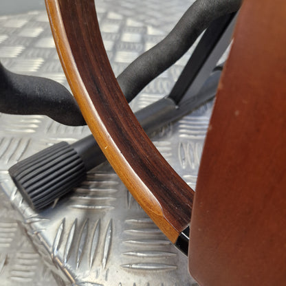 Pre-Owned Yamaha SLG200S Silent Guitar Electro-Acoustic - Natural Close-up of a wooden chair or stool showing a curved reddish-brown wood frame, a black plastic footrest, and a textured silver metal surface underneath.