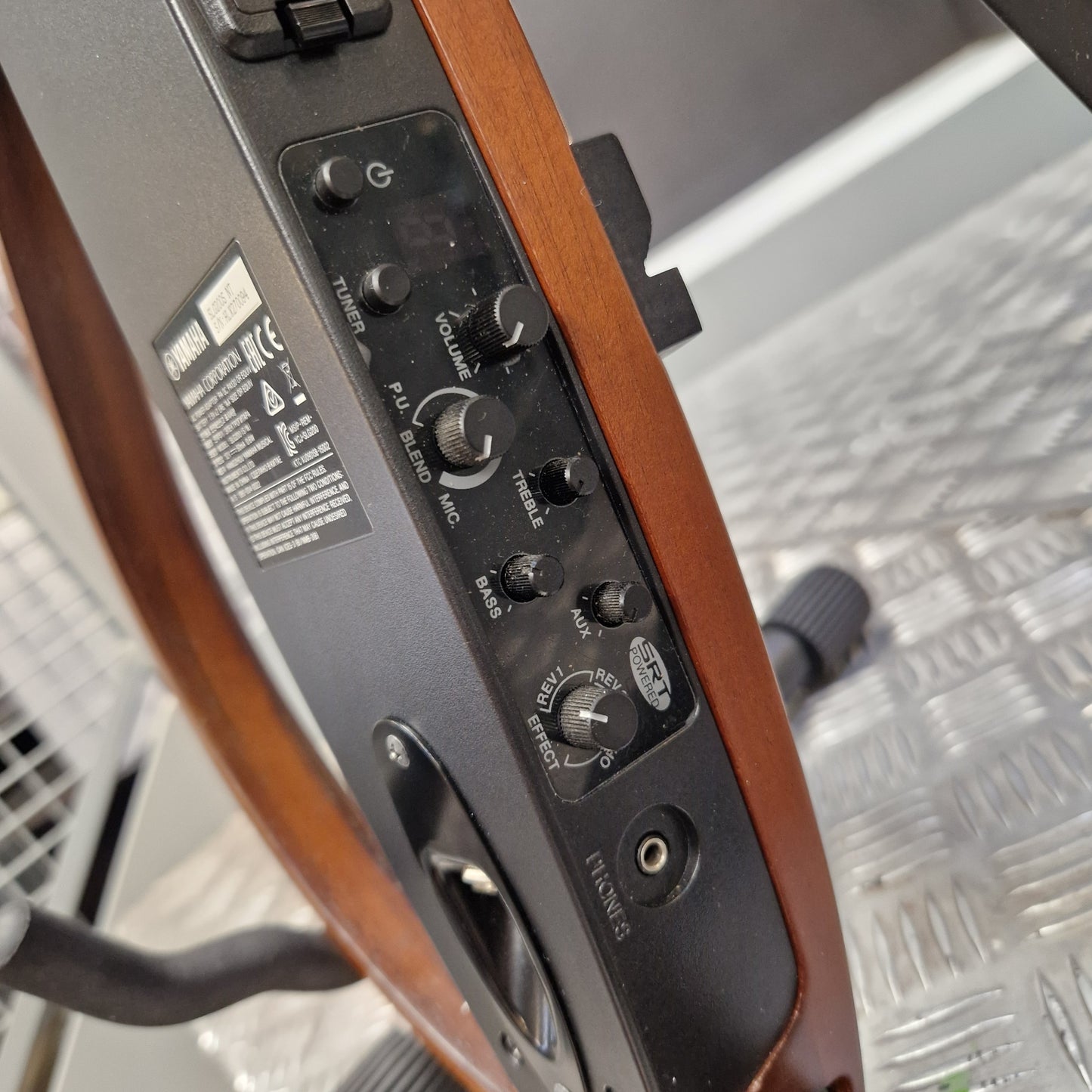 Pre-Owned Yamaha SLG200S Silent Guitar Electro-Acoustic - Natural Close-up of the control panel of a Yamaha speaker, showing various knobs and labels like PA, RELAY, MUTE, and SPEAKER, mounted on a wooden structure over a diamond plate metal floor.