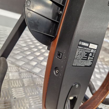 Pre-Owned Yamaha SLG200S Silent Guitar Electro-Acoustic - Natural Close-up of the side and back of a Yamaha exercise machine, showing the black plastic frame, wood trim, and a Yamaha specification label on a metal treadle floor.