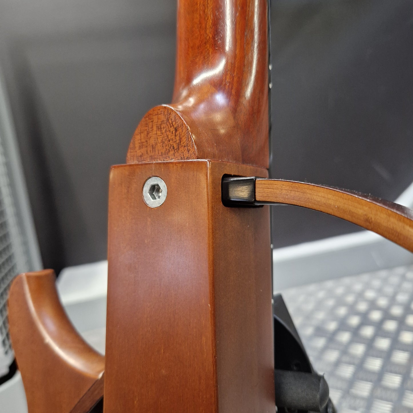 Pre-Owned Yamaha SLG200S Silent Guitar Electro-Acoustic - Natural Close-up of a polished reddish-brown wooden rifle stock with a visible screw and a leather sling strap attached, photographed indoors against a dark gray background.