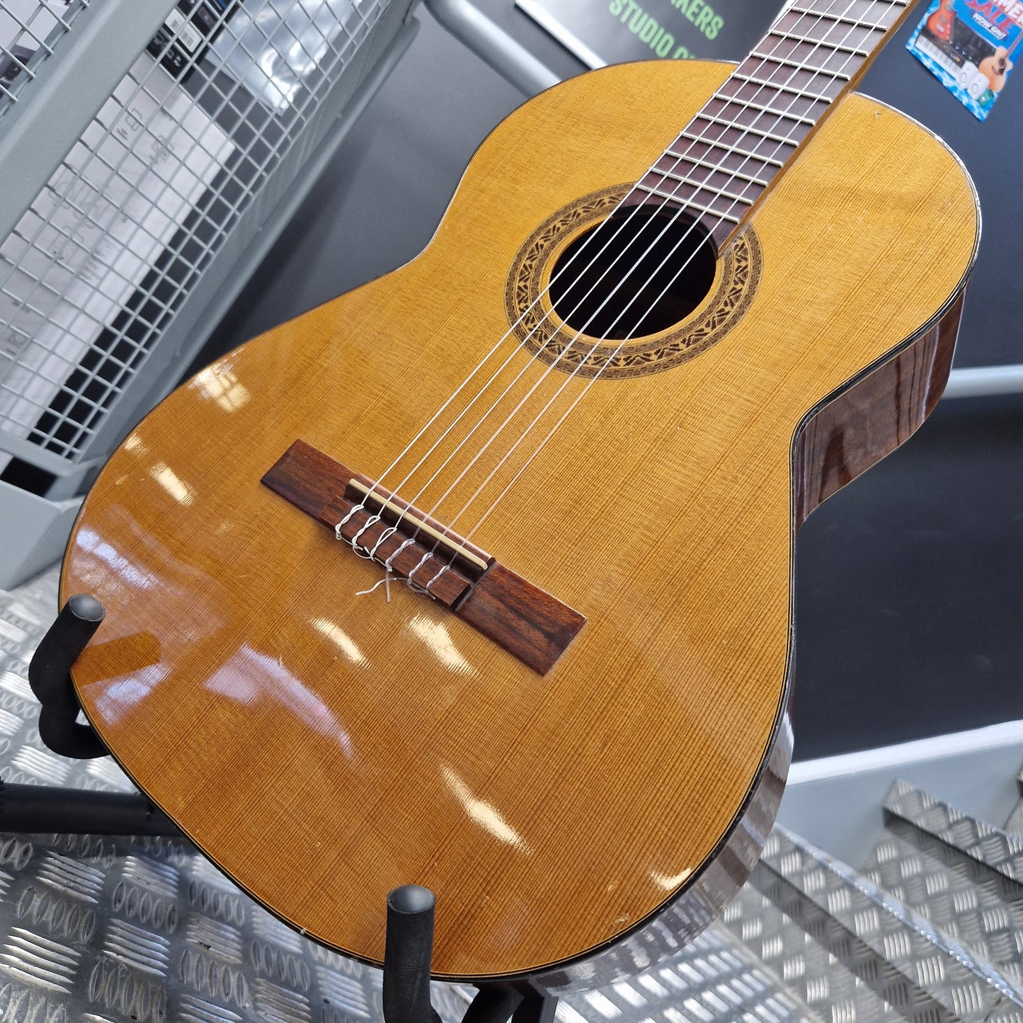 Pre-Owned Admira Solista Classical - Natural A close-up of a classical guitar body made from natural wood, showing the grain, sound hole, bridge, and part of the neck, displayed on a stand in what appears to be a workshop or studio.