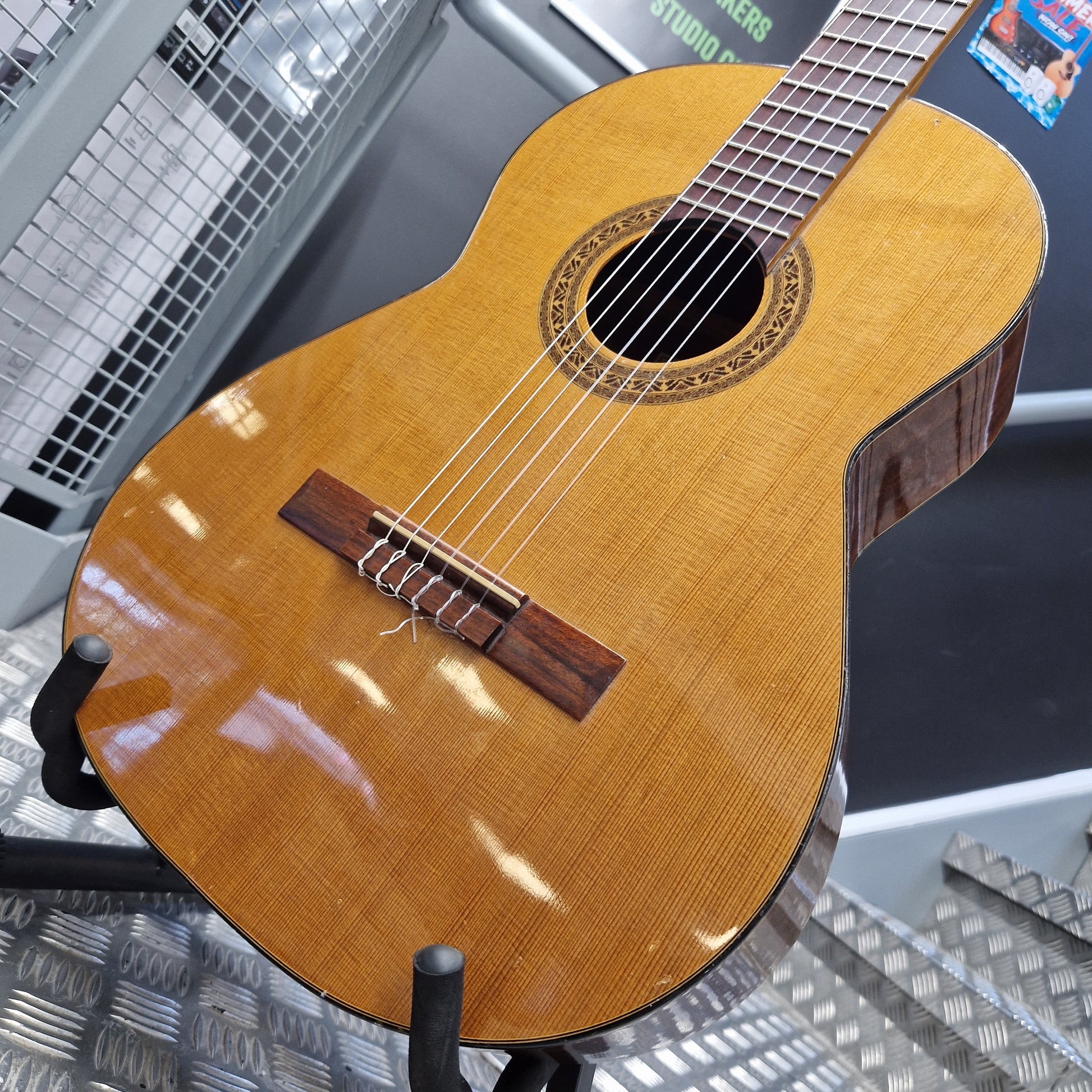 Pre-Owned Admira Solista Classical - Natural A close-up of a classical guitar body made from natural wood, showing the grain, sound hole, bridge, and part of the neck, displayed on a stand in what appears to be a workshop or studio.