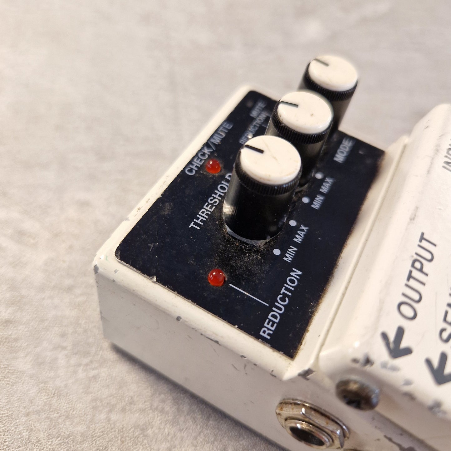 Pre-Owned Boss NS-2 Noise Suppressor Pedal A close-up of a used electric guitar effects pedal, specifically a Wah-Wah or Wah-Tech style overdrive with three black and white rotary knobs, red LED indicator lights, and a white plastic casing on a textured gray background.
