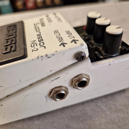 Pre-Owned Boss NS-2 Noise Suppressor Pedal Close-up of a used Boss NS-2 guitar effects pedal, showing the white metal casing, black knobs, and printed specifications on the top plate.