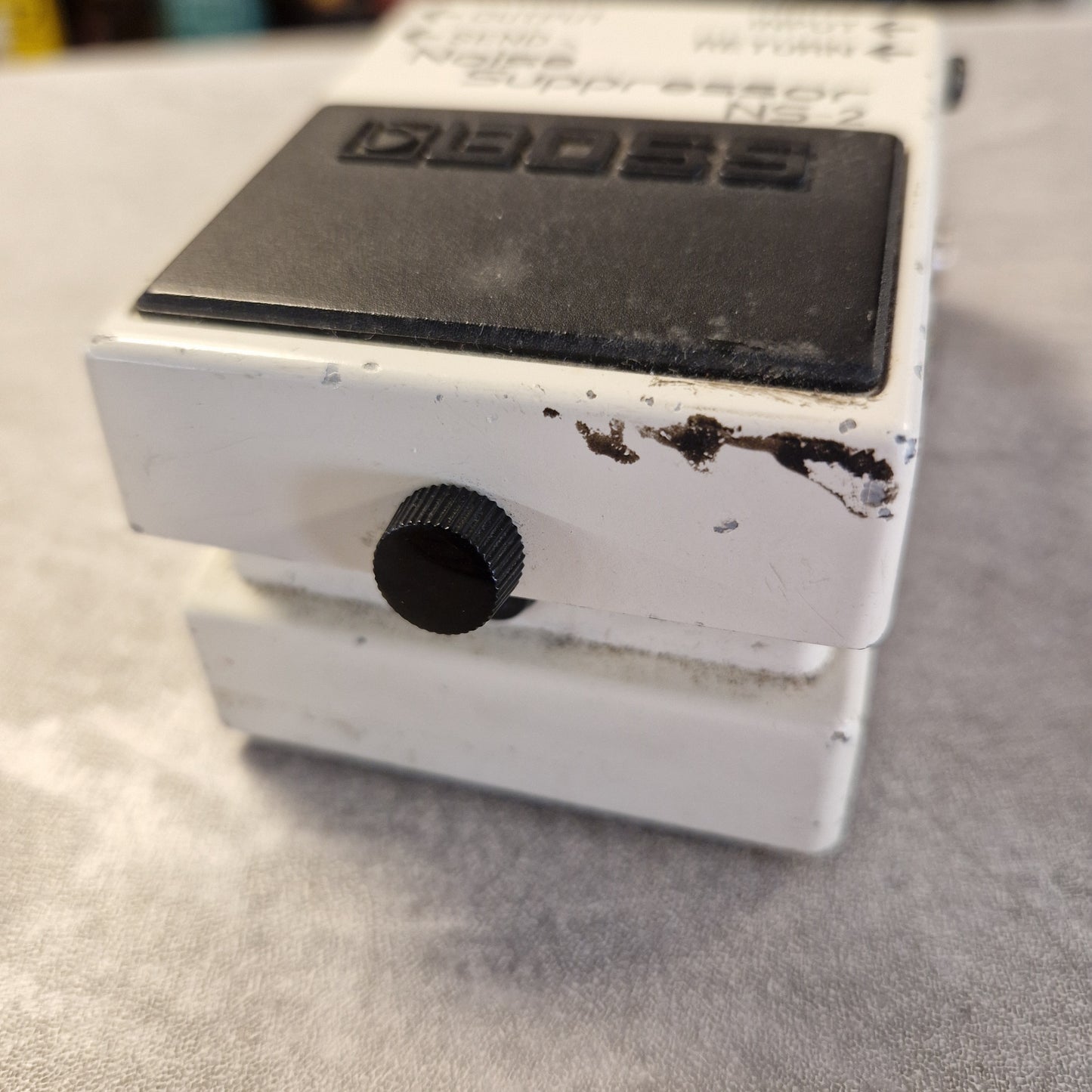 Pre-Owned Boss NS-2 Noise Suppressor Pedal A used white and black Boss Noise Suppressor NS-2 guitar pedal with visible scuffs and dirt on the front, resting on a gray textured surface.