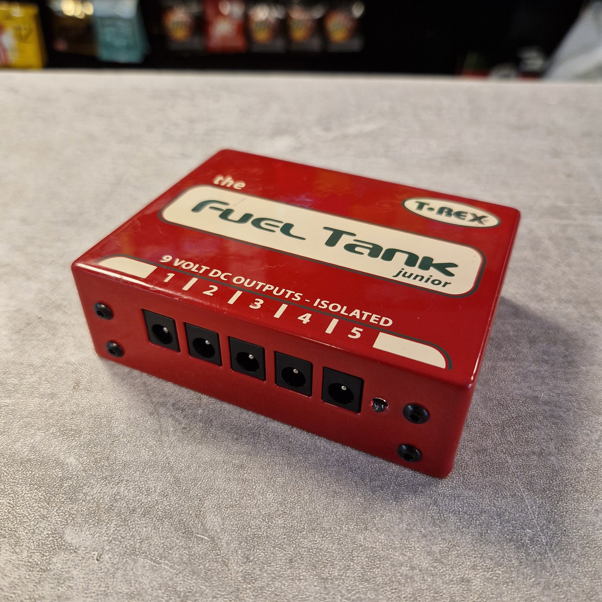Pre-Owned T. Rex Fuel Tank Junior Power Supply A red T-Nex Fuel Tank Junior 9V DC output power supply, photographed on a textured gray surface with a blurred background.