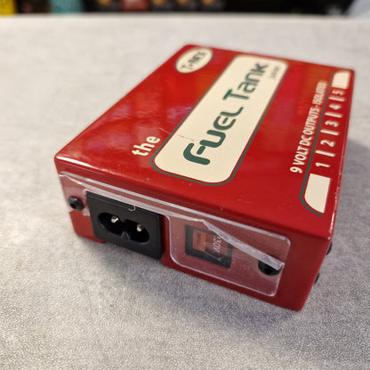 Pre-Owned T. Rex Fuel Tank Junior Power Supply A red electronic module labeled 'Fuel Tank' with a power input socket and a switch, photographed on a gray textured surface.