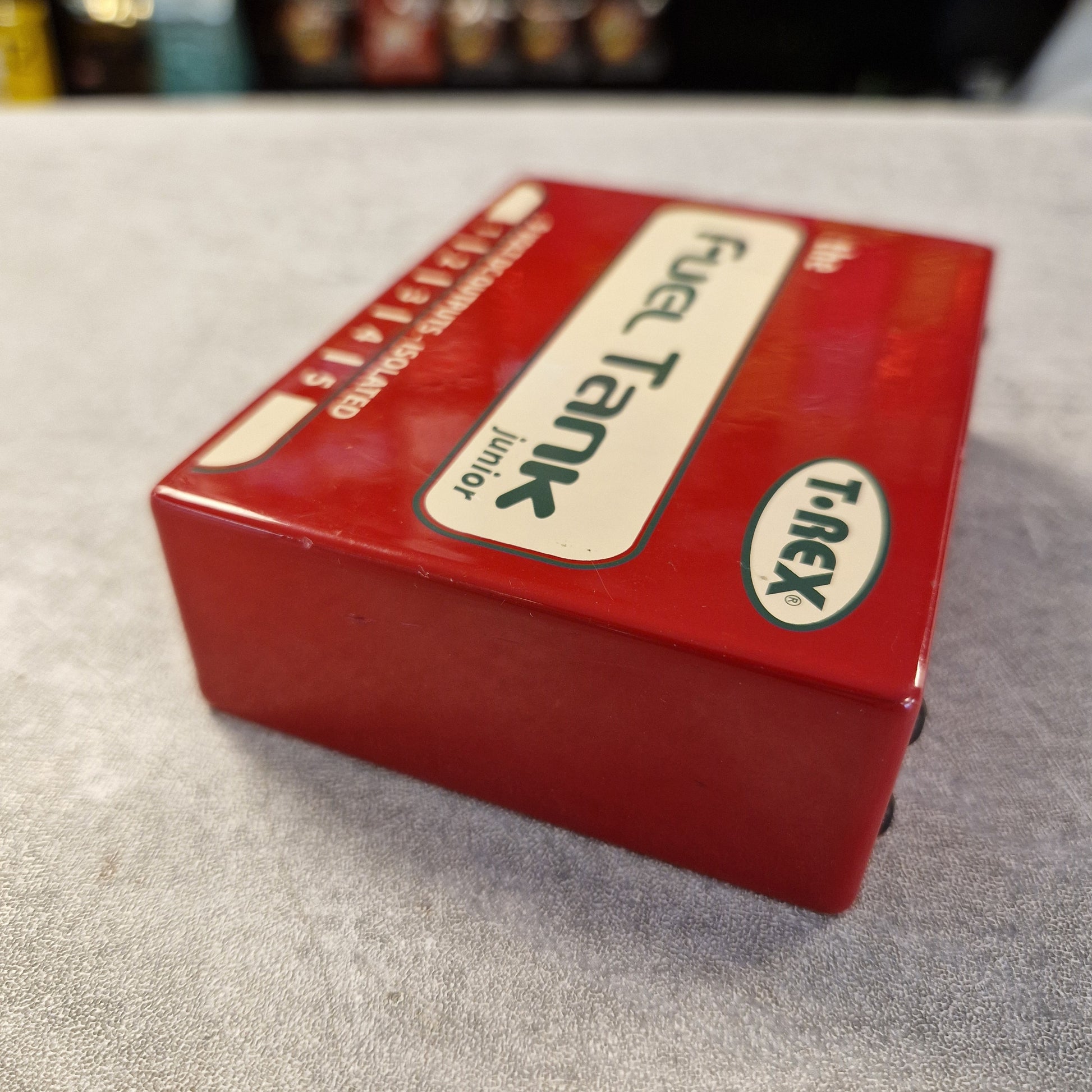Pre-Owned T. Rex Fuel Tank Junior Power Supply A red T-rex brand Fuel Tank Junior model kit box, photographed on a gray textured surface with a blurred background.