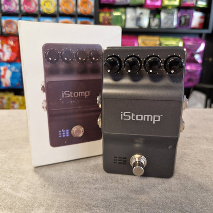 Pre-Owned DigiTech iStomp Switchable Multi Guitar Effects Pedal A black iStomp guitar effects pedal stands in front of its white retail box on a gray tabletop. The pedal has five black rotary knobs, a silver foot switch, and the iStomp logo printed in white on the front.