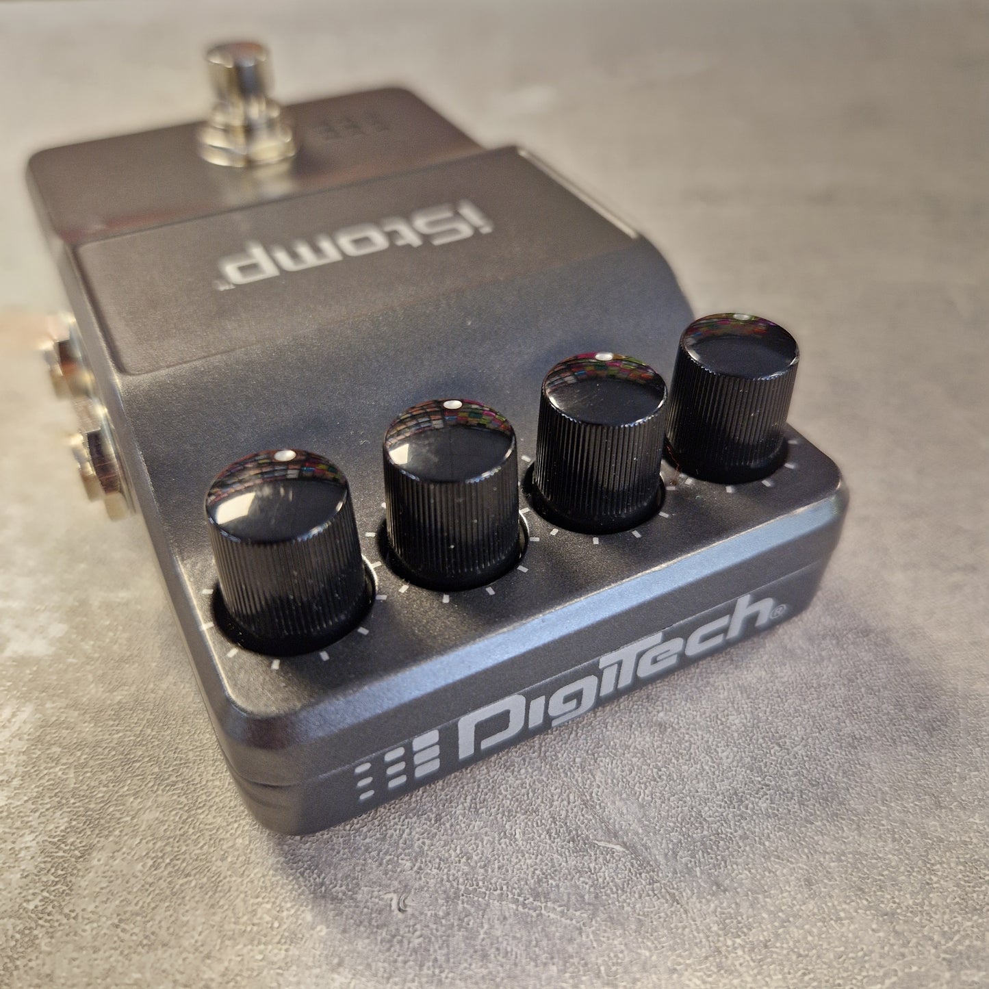 Pre-Owned DigiTech iStomp Switchable Multi Guitar Effects Pedal A Digitech Stomp guitar effects pedal with a dark gray metal body, four black control knobs, and a silver footswitch, photographed on a textured gray surface.