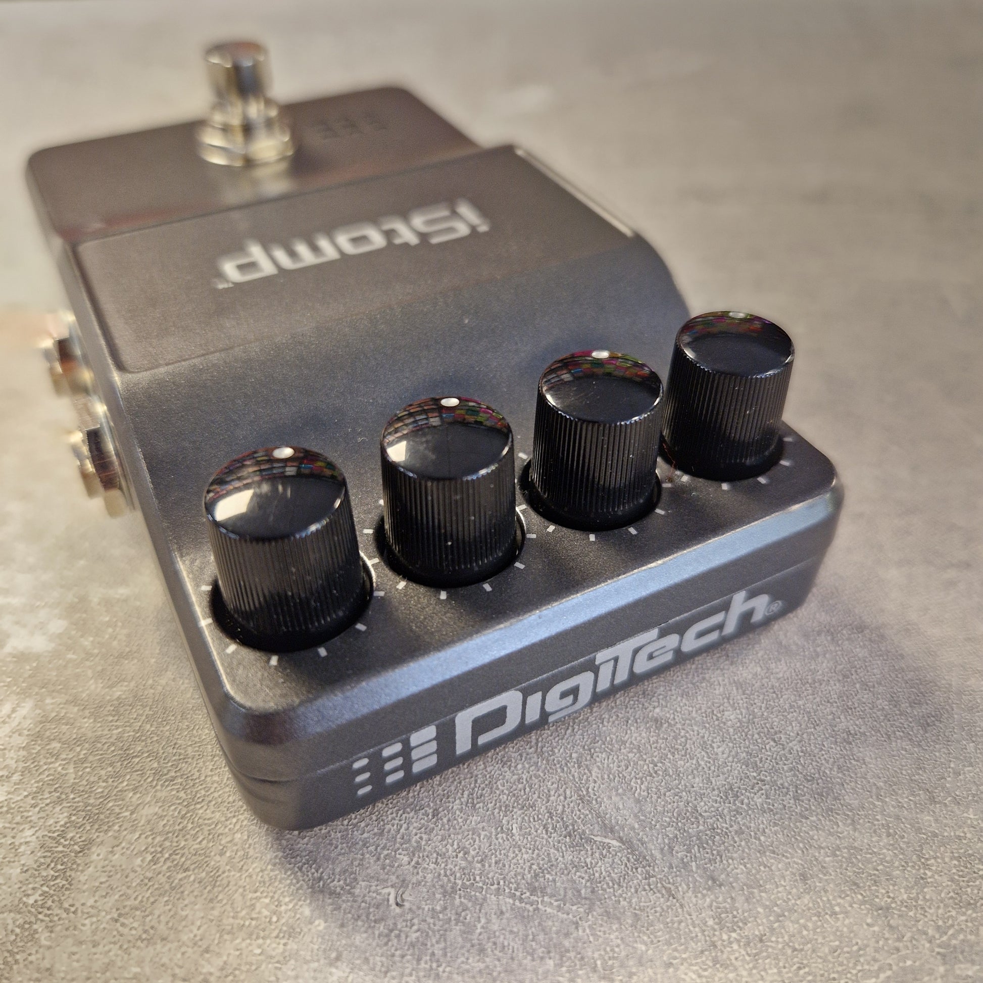 Pre-Owned DigiTech iStomp Switchable Multi Guitar Effects Pedal A Digitech Stomp guitar effects pedal with a dark gray metal body, four black control knobs, and a silver footswitch, photographed on a textured gray surface.