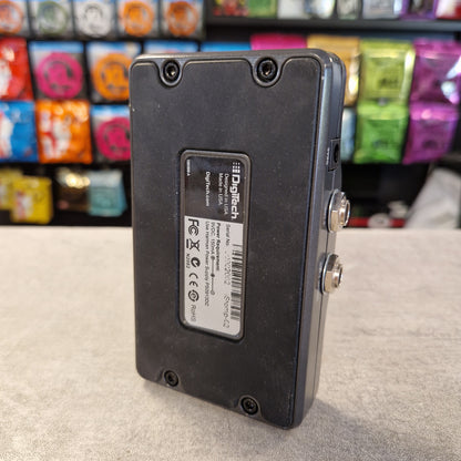 Pre-Owned DigiTech iStomp Switchable Multi Guitar Effects Pedal A black Digitech MP310 digital multi-effects pedal shown from the back, featuring a white product label with barcodes and specifications, set on a gray tabletop with a blurred background of colorful store shelves.