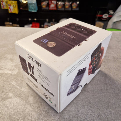 Pre-Owned DigiTech iStomp Switchable Multi Guitar Effects Pedal A white retail box for the iStomp pedal by iFluxx, showing product photos and specifications on a gray tabletop with a blurred store background.