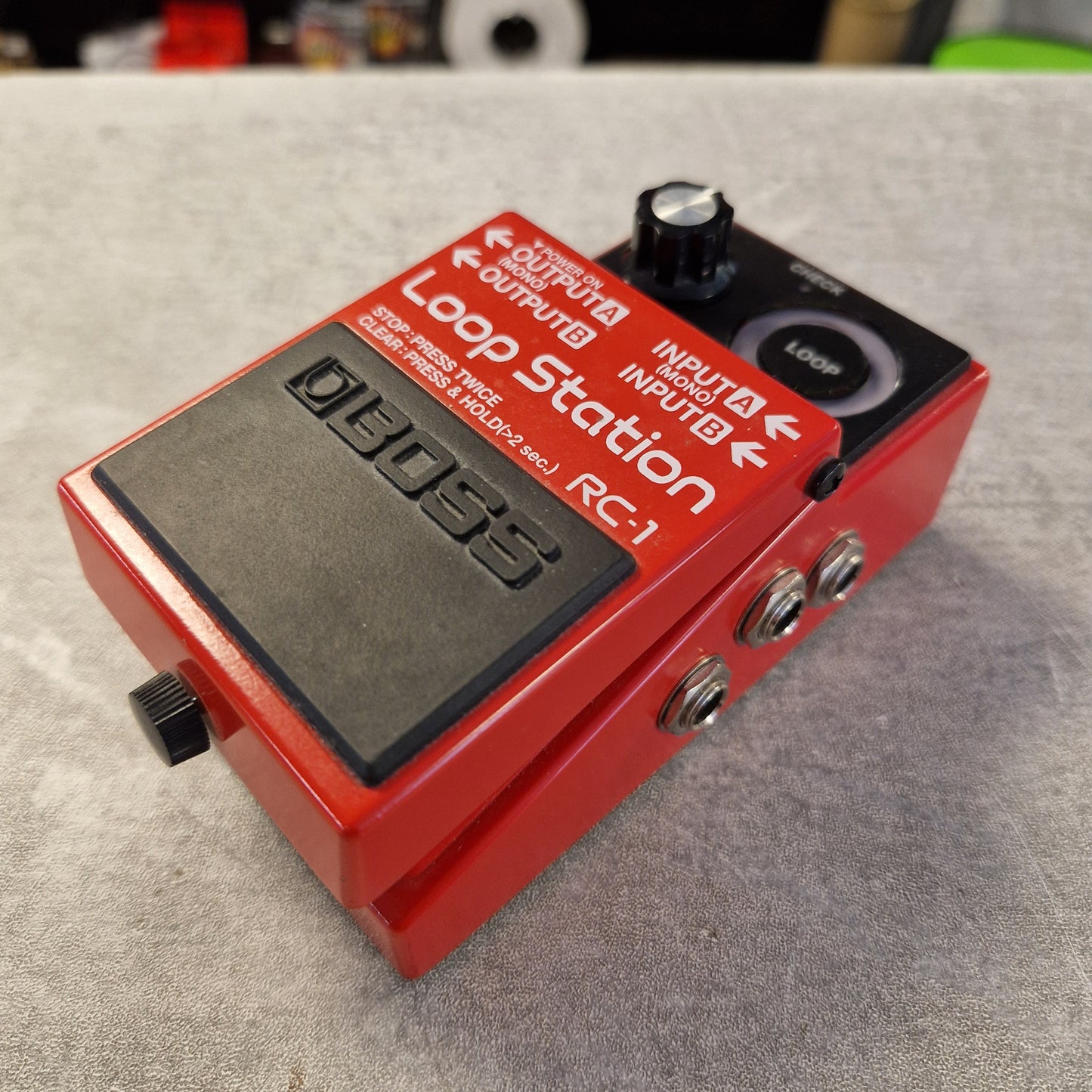 Pre-Owned Boss RC-1 Loop Station Pedal A red Boss RC-1 Loop Station guitar effects pedal with black controls and silver metal jacks, photographed on a gray textured surface.