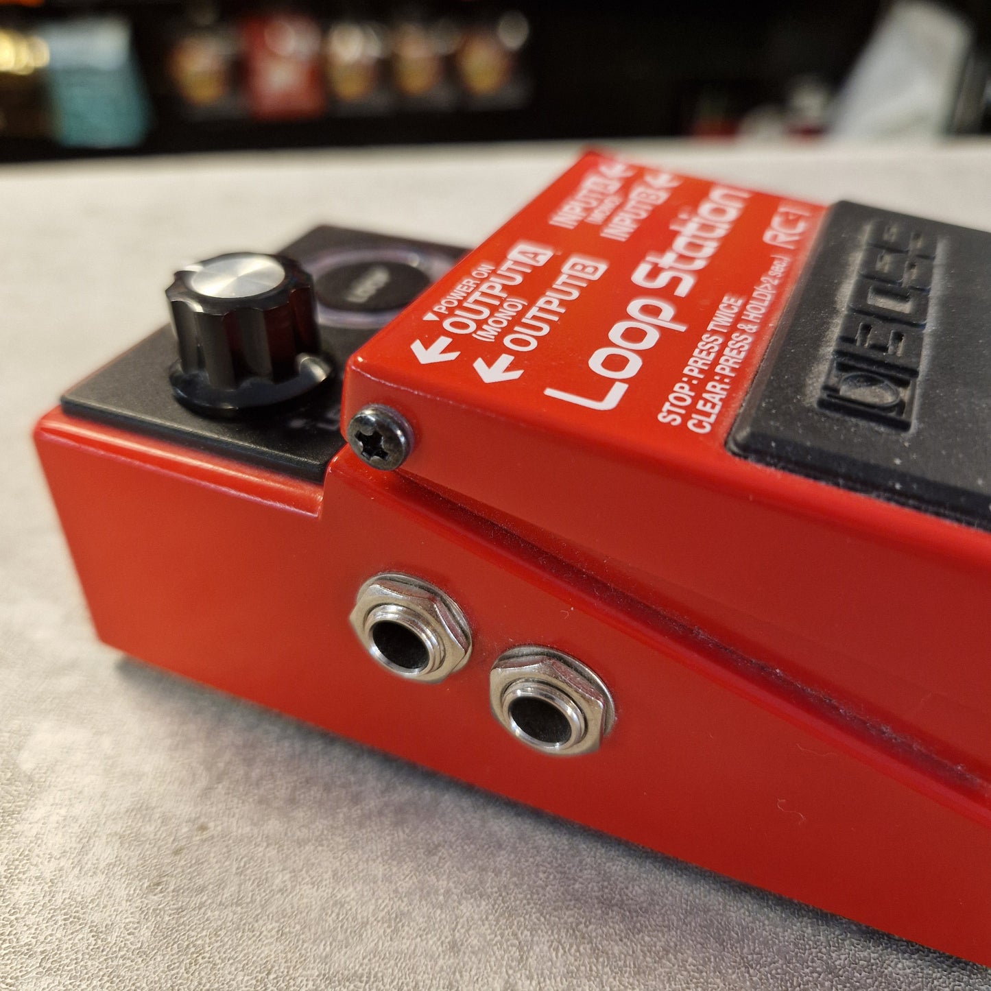 Pre-Owned Boss RC-1 Loop Station Pedal A close-up shot of a red and black Loop Station pedal guitar effect, showing its knobs and jacks on a gray surface.