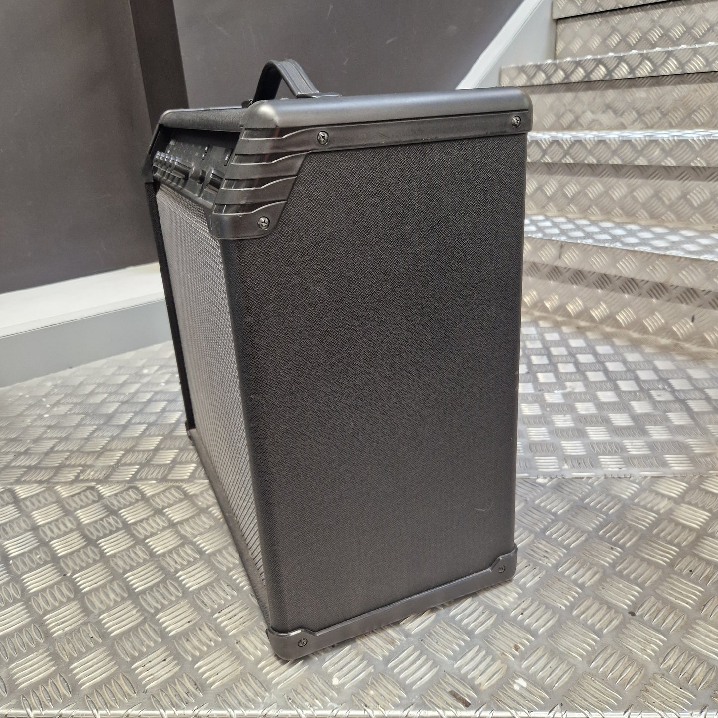 Pre-Owned Line 6 Spider V 120 Mk II Guitar Combo Amplifier A black guitar amplifier with a textured front grille and protective metal corners, positioned on a diamond plate metal staircase.