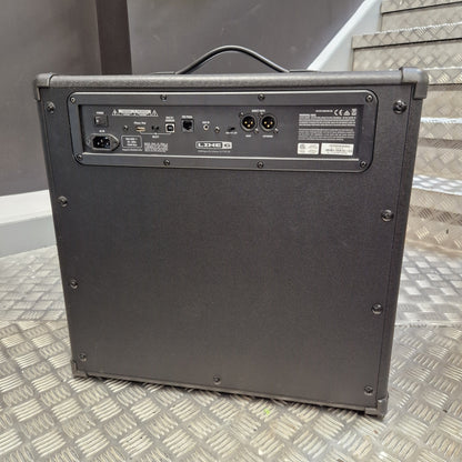 Pre-Owned Line 6 Spider V 120 Mk II Guitar Combo Amplifier A black guitar amplifier or speaker cabinet photographed from the back, standing on a diamond-plate metal floor with stairs in the background.