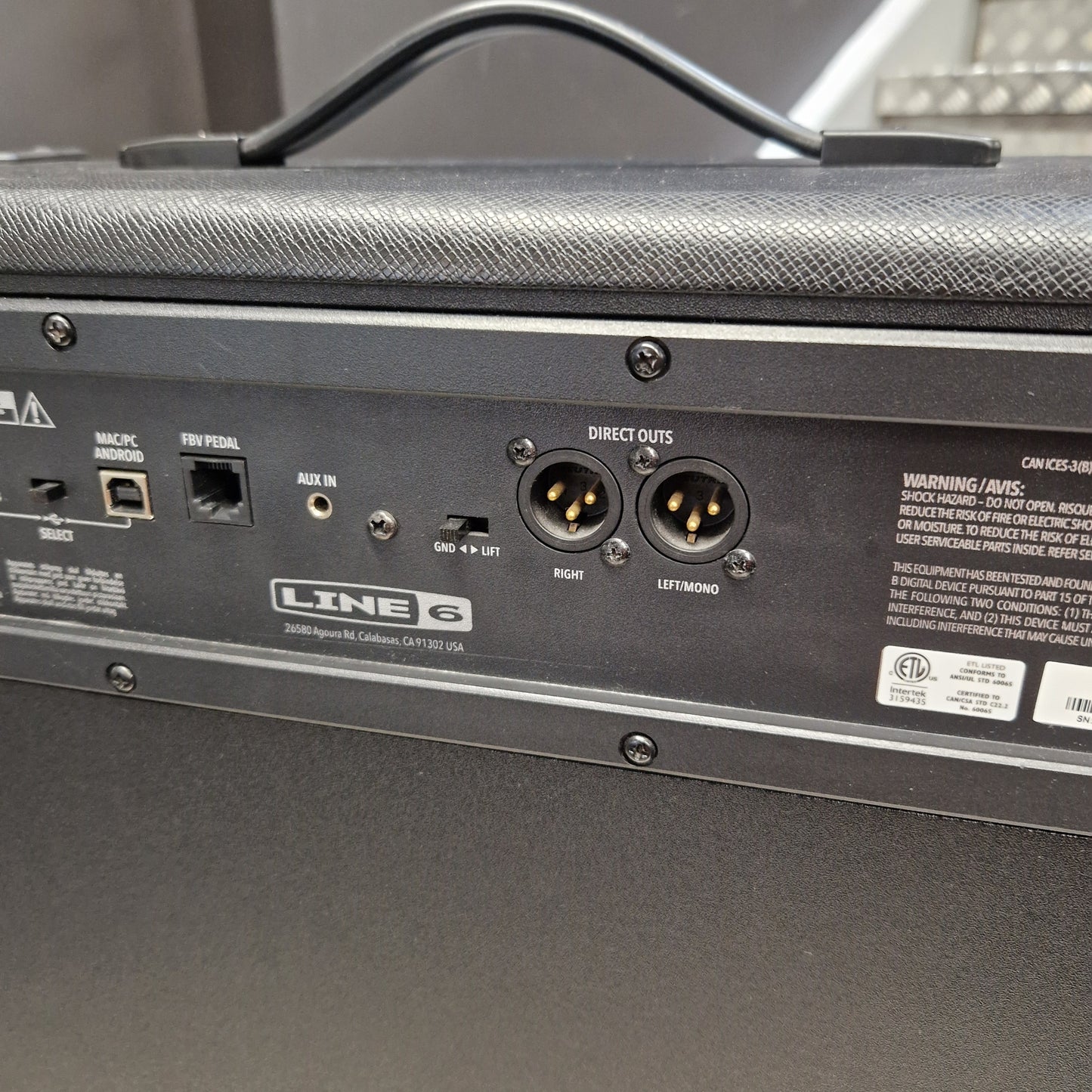 Pre-Owned Line 6 Spider V 120 Mk II Guitar Combo Amplifier Close-up of the rear panel of a black Line 6 mobile amplifier, showing input and output jacks, labels, and a handle on top.