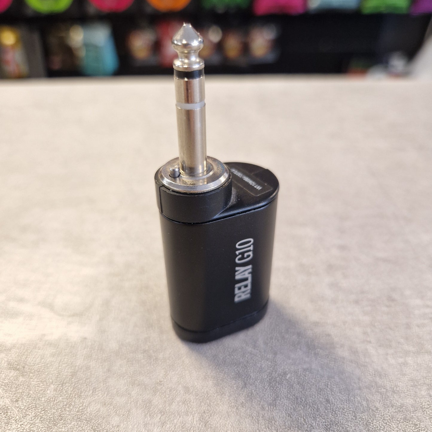Pre-Owned Line 6 Spider V 120 Mk II Guitar Combo Amplifier A black RELN G10 audio adapter with a silver 1/4-inch jack plug, standing on a gray textured surface with a blurred background.