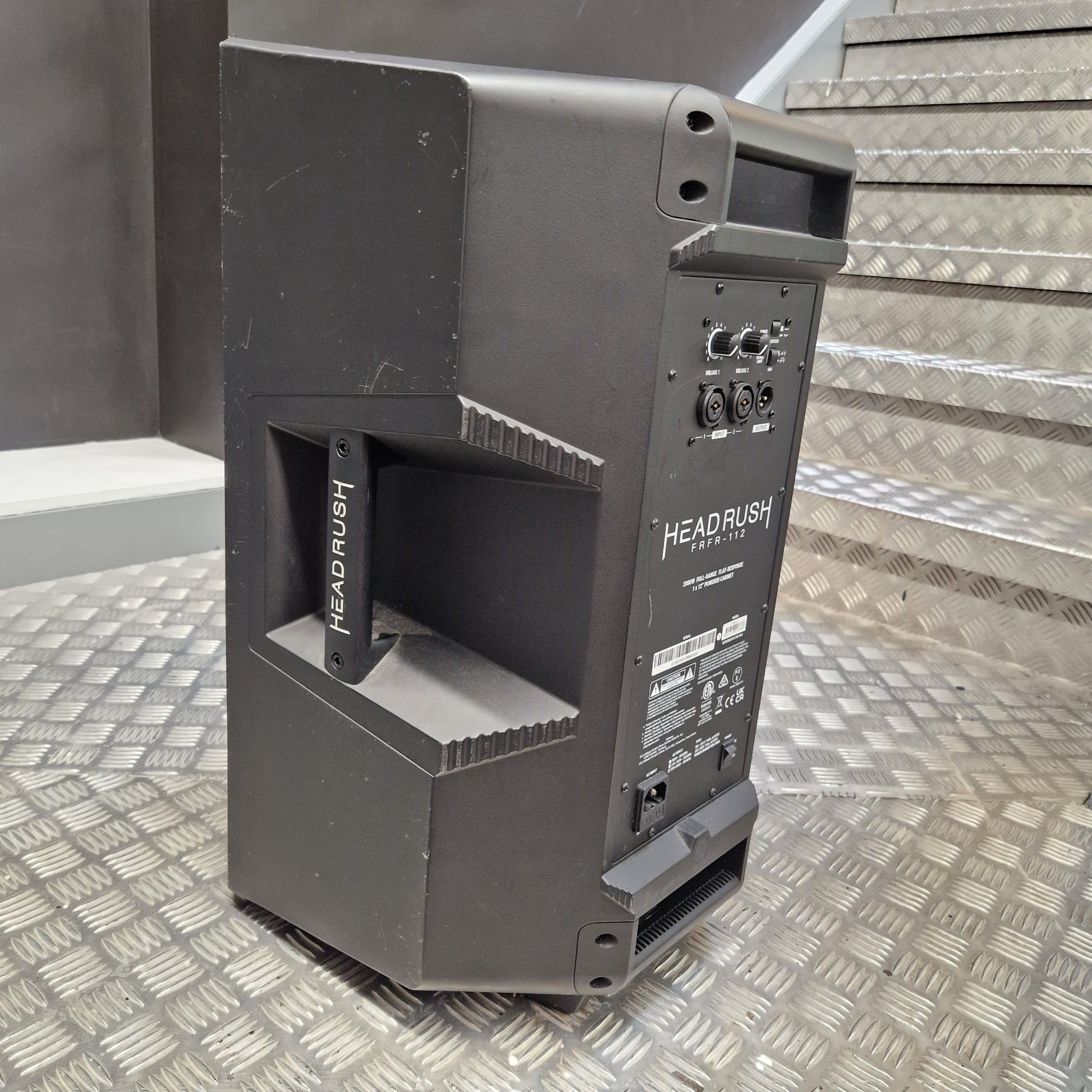 Pre-Owned Headrush FRFR-112 Full Range Powered 1x12 Speaker A black HENKUAI Headrush 15 portable speaker shown from the rear, positioned on a diamond plate metal staircase.