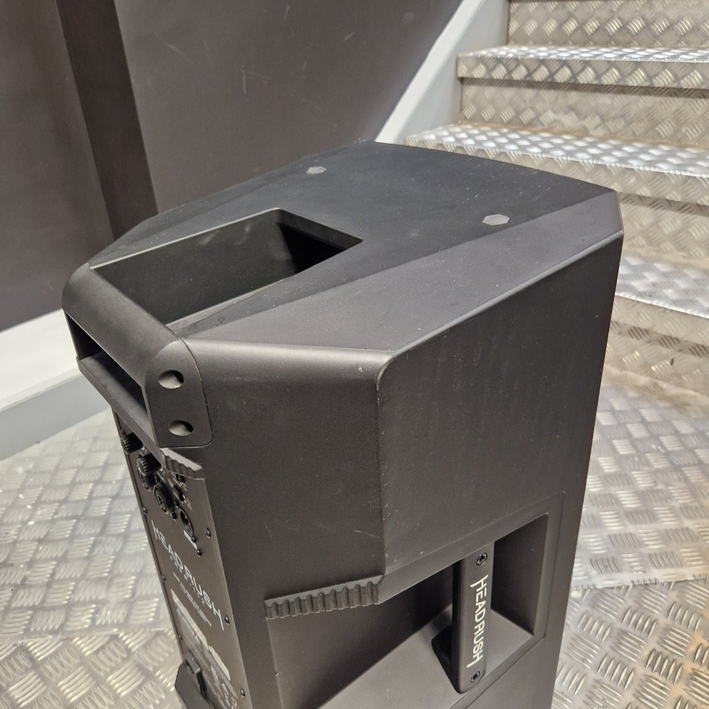 Pre-Owned Headrush FRFR-112 Full Range Powered 1x12 Speaker A black Festoon portable speaker shown from an angled top-down view, resting on a diamond plate metal staircase.