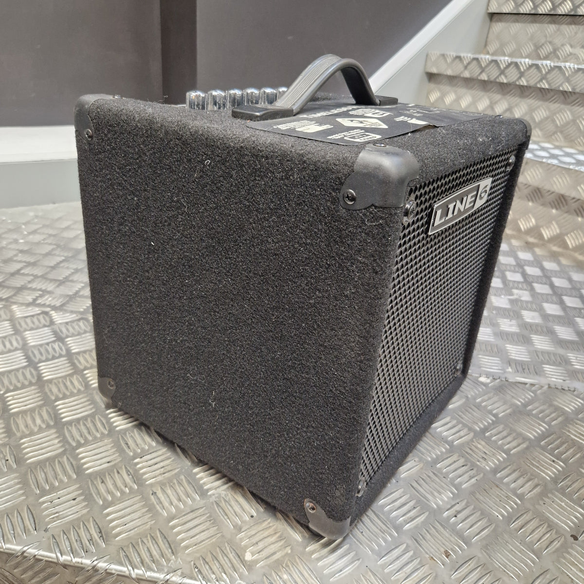 Pre-Owned Line 6 LowDown Studio 110 75w Digital Bass Combo A black Line 6 DSL1500 guitar amplifier speaker cabinet with a textured fabric cover and metal grille, resting on a diamond plate metal surface.