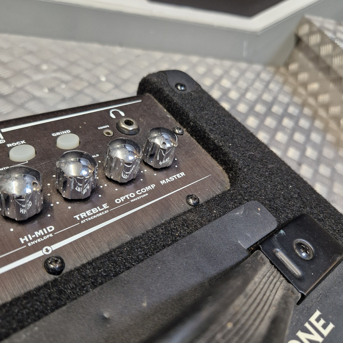 Pre-Owned Line 6 LowDown Studio 110 75w Digital Bass Combo Close-up of a black and silver guitar effects pedal or amplifier control panel with knobs labeled HI-MID, SMITH, TREBLE, OPTO COMP, and MASTER, resting on a textured metal surface.