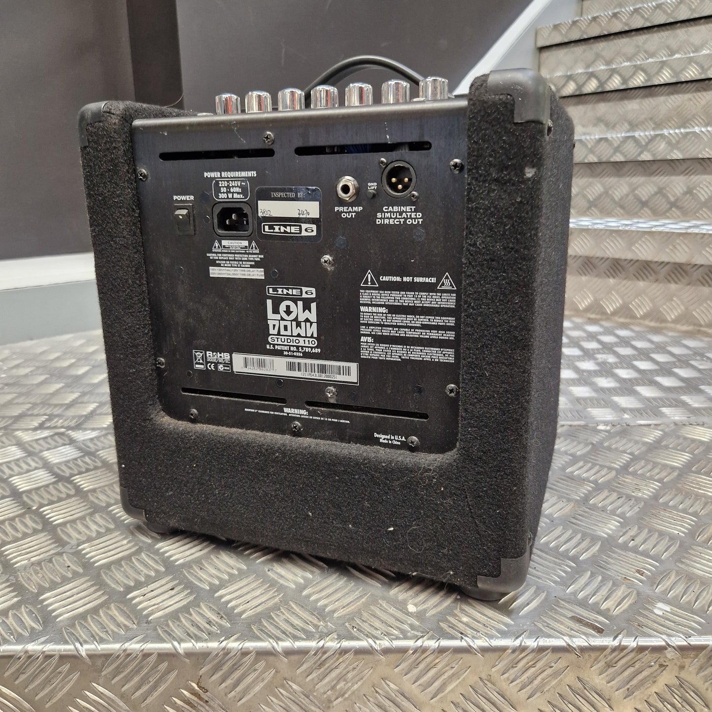 Pre-Owned Line 6 LowDown Studio 110 75w Digital Bass Combo The rear view of a black Lowman 120W portable guitar amplifier, showing its various input and output jacks, set on a diamond plate metal surface.