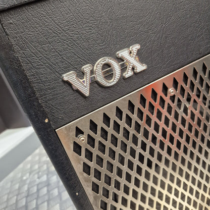 Pre-Owned Vox VT100 Valvetronix 100w Electric Combo Close-up of a black textured Vox amplifier or speaker cabinet with a silver metal grille and a prominent silver VOX logo badge.