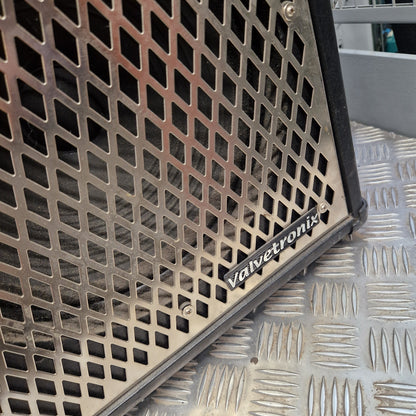 Pre-Owned Vox VT100 Valvetronix 100w Electric Combo Close-up of a metal mesh speaker grille with a black frame and a visible 'valvetronix' badge, resting on a diamond-plate metal surface.